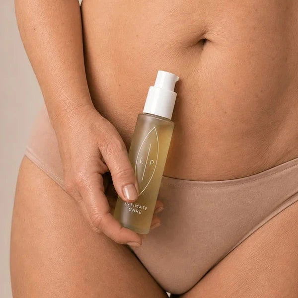 A close-up of a woman holding a clear pump bottle filled with golden liquid- cleansing and soothing oil fro dryness during menopause.