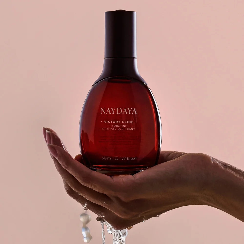 A hand holds a bottle of NAYDAYA Victory Glide water-based lubricant and vaginal moisturiser for menopause and perimenopause, designed to support intimate hydration and comfort.