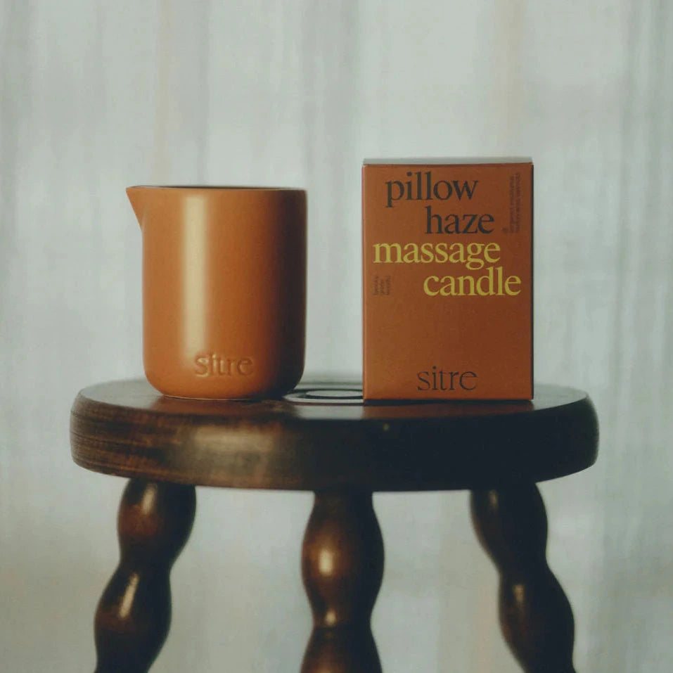 Sitre Massage Candle and its packaging on a wooden stool with a white curtain background